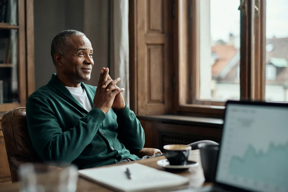 Inbound Marketing Expert: Anfragen, die Sie erreichen Mann mit grauem Kurzhaar im grünen Cardigan sitzt lächelnd am Fenster, vor ihm ein Laptop mit steigender Kurve.